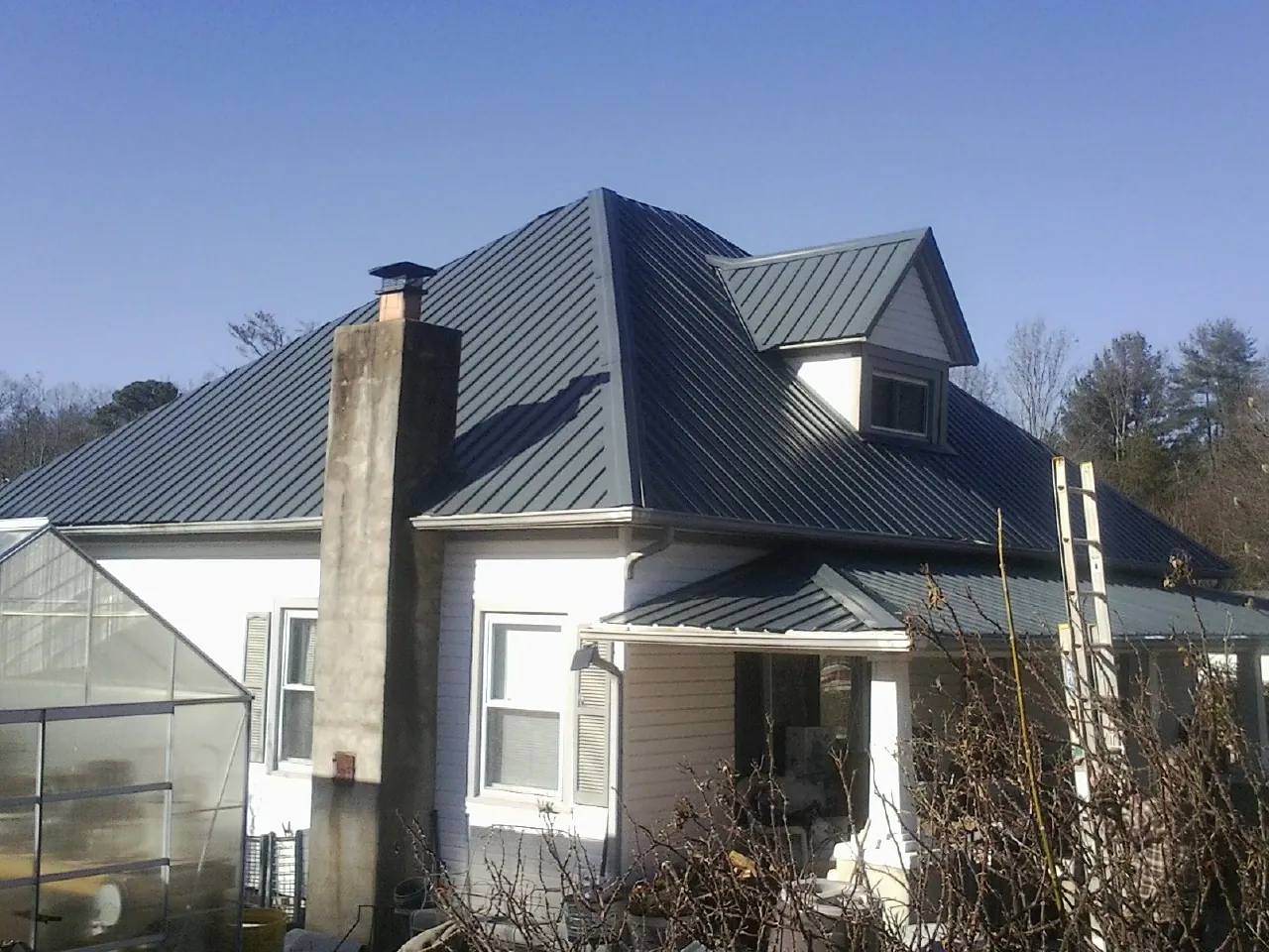 Dark blue standing seam metal roof on a white farmhouse with dormer — Slate & Tile Roof Repair by Roofing Brothers in Whittier