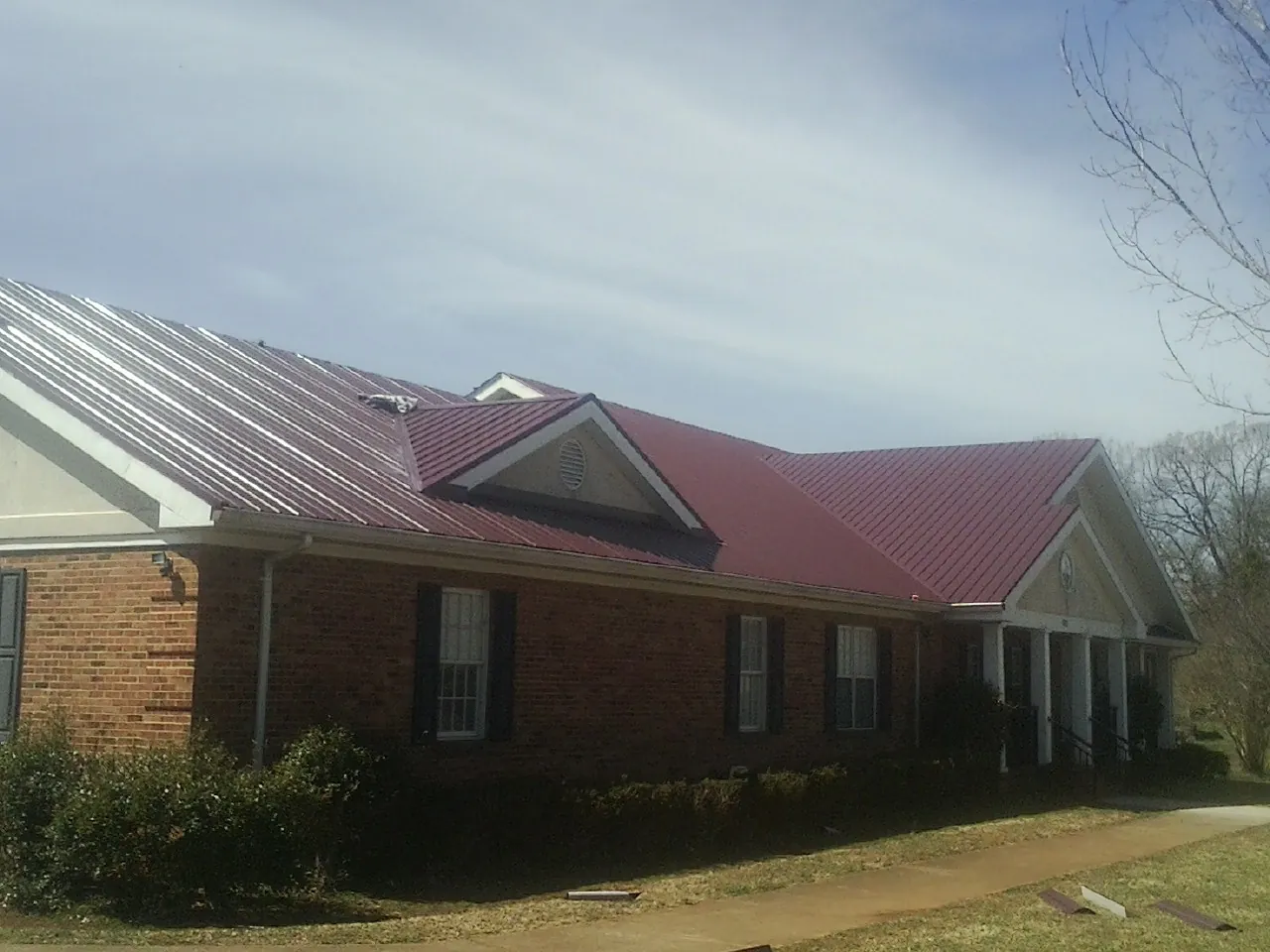 Red metal roof with gabled entries on a long brick building, from a Hail Damage Roof Repair job in Whittier