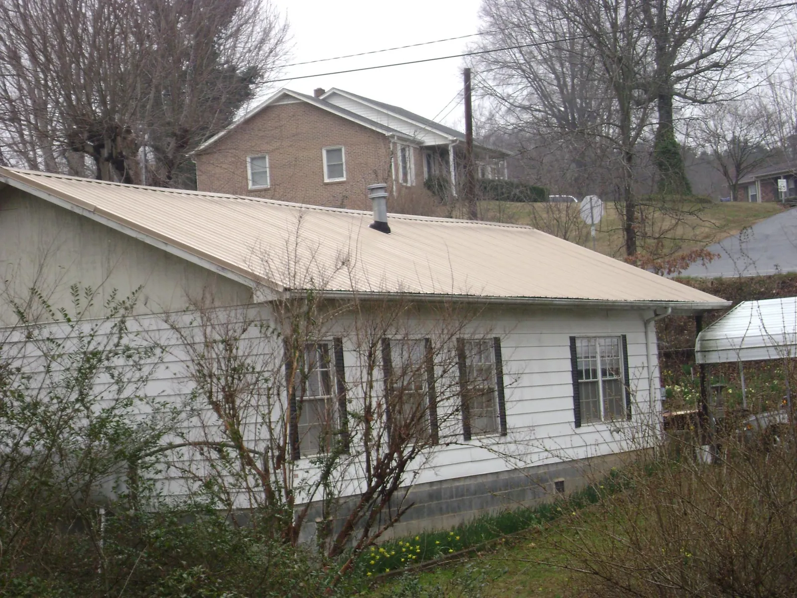 Tan metal roof on a white sided house set into a hillside — Commercial Roofing by Roofing Brothers in Whittier